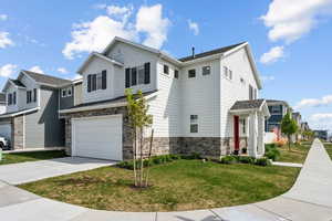 View of front of house featuring stone siding, an attached garage, driveway, and a front yard