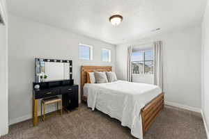 Bedroom featuring baseboards, dark colored carpet, a textured ceiling, and visible vents
