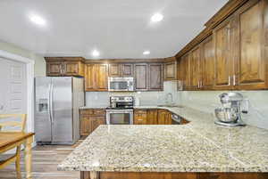 Kitchen featuring decorative backsplash, a sink, light stone counters, light wood finished floors, and stainless steel appliances