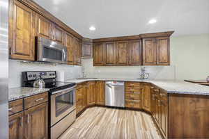 Kitchen with decorative backsplash, a peninsula, light stone countertops, a sink, and stainless steel appliances