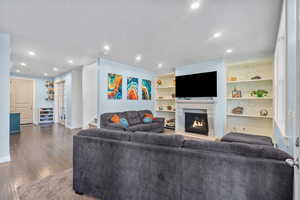 Living area featuring recessed lighting, a textured ceiling, dark wood-style flooring, and a glass covered fireplace
