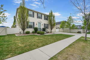 Colonial home with a front lawn, fence, stucco siding, a gate, and driveway