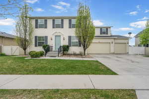 Colonial house featuring a gate, fence, a front lawn, concrete driveway, and stucco siding