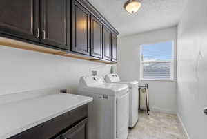 Clothes washing area with stone finish flooring, a textured ceiling, washing machine and clothes dryer, cabinet space, and baseboards