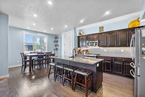 Kitchen featuring a breakfast bar, a sink, a kitchen island with sink, stainless steel appliances, and decorative backsplash
