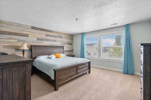 Bedroom with a textured ceiling, visible vents, wood walls, baseboards, and light carpet