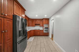 Kitchen with black appliances, tasteful backsplash, brown cabinets, light countertops, and recessed lighting