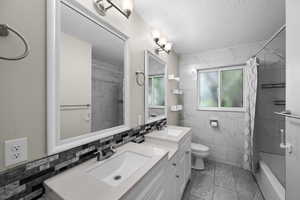 Bathroom featuring marble finish floors, a textured ceiling, tile walls, toilet, and double vanity