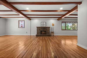 Unfurnished living room with wood finished floors, beam ceiling, baseboards, a fireplace, and recessed lighting