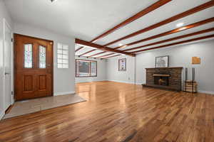 Foyer entrance with wood finished floors, a stone fireplace, beam ceiling, baseboards, and recessed lighting