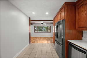 Kitchen with freestanding refrigerator, stainless steel dishwasher, wood finish floors, light countertops, and brown cabinets