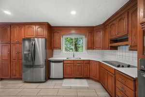 Kitchen featuring appliances with stainless steel finishes, a sink, backsplash, light countertops, and recessed lighting