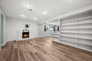 Unfurnished living room featuring baseboards, wood finished floors, a lit fireplace, and recessed lighting
