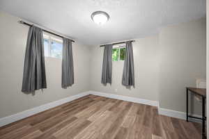 Unfurnished room with a textured ceiling, wood finished floors, and baseboards