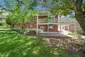 Back of property featuring brick siding, a patio, a lawn, and a deck