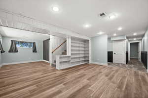 Basement with baseboards, wood finished floors, stairway, recessed lighting, and built in shelves