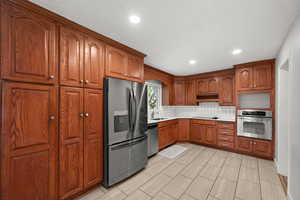 Kitchen with appliances with stainless steel finishes, tasteful backsplash, light countertops, recessed lighting, and brown cabinetry