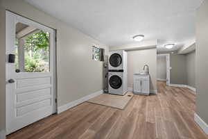 Washroom with cabinet space, stacked washing machine and dryer, light wood-style floors, baseboards, and a textured ceiling