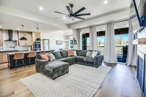 Living area featuring light wood-type flooring, recessed lighting, ceiling fan with notable chandelier, and a fireplace