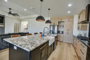 Kitchen featuring wall chimney range hood, a sink, stainless steel fridge with ice dispenser, light brown cabinets, and light wood-style flooring