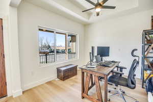 Office area featuring ceiling fan, a raised ceiling, arched walkways, baseboards, and light wood-type flooring