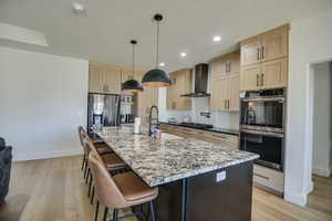 Kitchen with light brown cabinets, baseboards, wall chimney exhaust hood, a sink, and stainless steel appliances