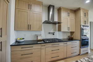 Kitchen featuring dark countertops, light brown cabinetry, stainless steel appliances, and wall chimney exhaust hood