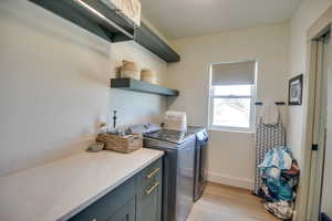 Laundry room with baseboards, light wood finished floors, cabinet space, and washing machine and clothes dryer