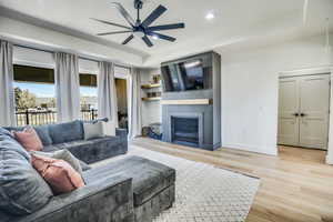 Living area featuring ceiling fan, a large fireplace, baseboards, and light wood-type flooring