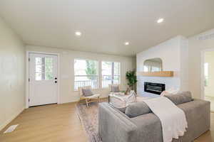 Living room with a fireplace, recessed lighting, light wood-style flooring, and visible vents