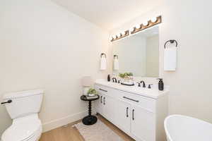 Full bathroom with double vanity, a freestanding bath, wood finished floors, a sink, and toilet