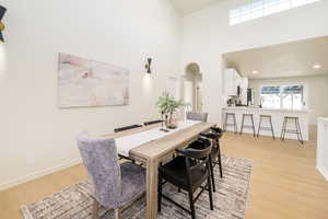 Dining room featuring a high ceiling, arched walkways, recessed lighting, baseboards, and light wood-type flooring