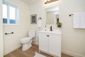 Bathroom featuring baseboards, wood finished floors, toilet, and vanity