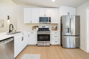 Kitchen featuring light wood-style floors, a sink, white cabinetry, and appliances with stainless steel finishes