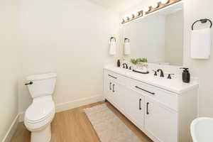 Bathroom with a sink, double vanity, toilet, baseboards, and wood finished floors