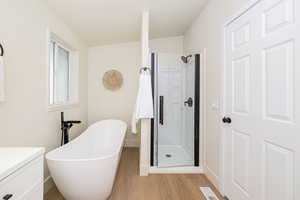 Full bath with visible vents, vanity, wood finished floors, a freestanding bath, and a stall shower