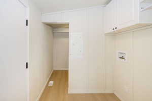 Clothes washing area with washer hookup, electric panel, visible vents, cabinet space, and light wood-style floors