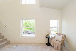 Living area with carpet floors, high vaulted ceiling, a healthy amount of sunlight, visible vents, and stairway