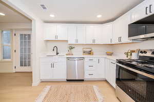 Kitchen featuring appliances with stainless steel finishes, a sink, light wood-style floors, light countertops, and visible vents