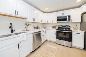 Kitchen featuring light countertops, white cabinetry, a sink, light wood finished floors, and appliances with stainless steel finishes