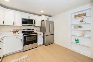 Kitchen featuring light wood-type flooring, light countertops, recessed lighting, white cabinets, and stainless steel appliances