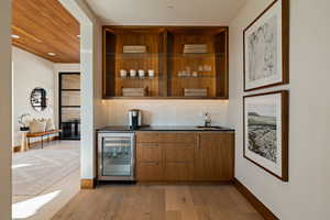 Indoor wet bar featuring beverage cooler, light wood finished floors, tasteful backsplash, and baseboards