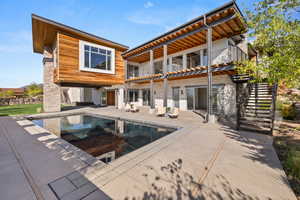 Rear view of property with a balcony, a patio, an outdoor pool, and stairs