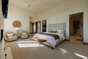 Carpeted bedroom featuring baseboards, a fireplace, a towering ceiling, and ensuite bath