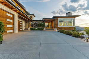 View of front of house with stone siding, driveway, and a chimney