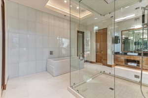 Bathroom with a tray ceiling, tile walls, a shower stall, and tile patterned flooring