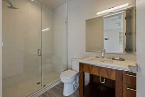 Bathroom with a stall shower, toilet, wood finished floors, and vanity