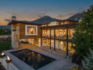 Back of house at dusk featuring a balcony, a chimney, a mountain view, stone siding, and a patio area