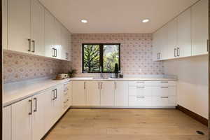 Kitchen with a sink, light wood-style floors, light countertops, tasteful backsplash, and white cabinetry