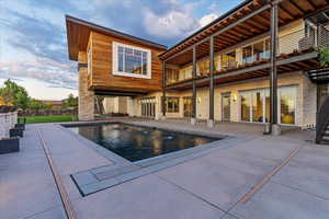 Back of house at dusk featuring an outdoor pool, a patio, and a balcony